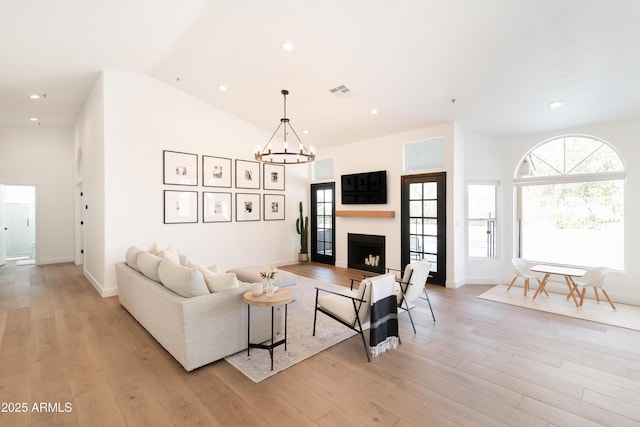 living area featuring a fireplace, light wood finished floors, lofted ceiling, visible vents, and a chandelier