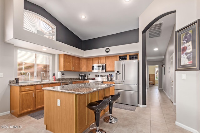 kitchen featuring appliances with stainless steel finishes, dark stone counters, sink, light tile patterned floors, and a center island