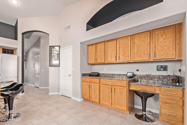 kitchen with dark stone countertops, light tile patterned floors, built in desk, and high vaulted ceiling