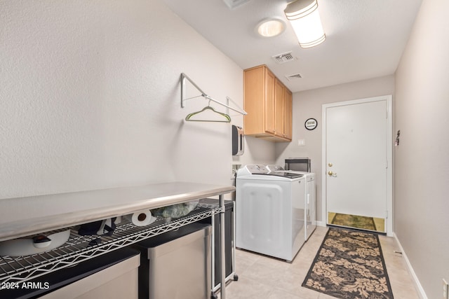 clothes washing area featuring washing machine and dryer, light tile patterned floors, and cabinets