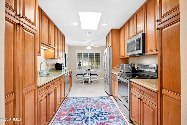 kitchen featuring ceiling fan, stainless steel appliances, a skylight, and sink