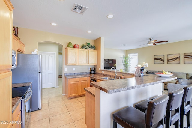 kitchen featuring a kitchen bar, light brown cabinetry, sink, appliances with stainless steel finishes, and kitchen peninsula