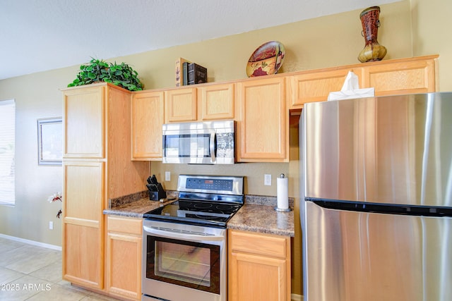 kitchen with dark stone countertops, stainless steel appliances, light tile patterned floors, and light brown cabinets