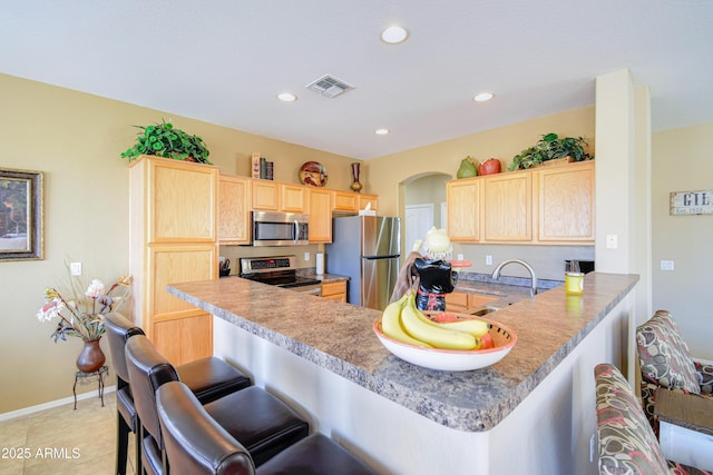 kitchen featuring a breakfast bar, sink, kitchen peninsula, stainless steel appliances, and light brown cabinets