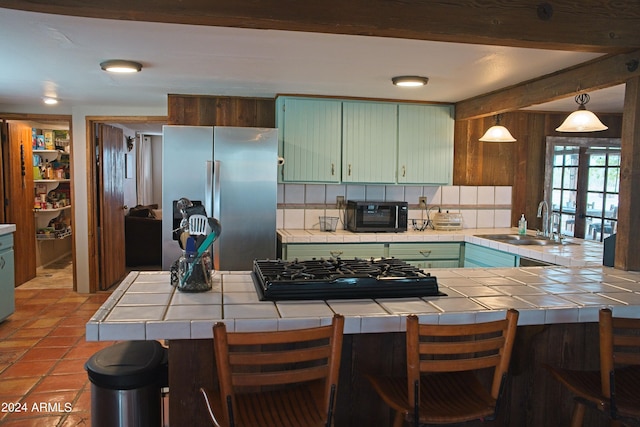 kitchen featuring a sink, beamed ceiling, black appliances, and tile counters