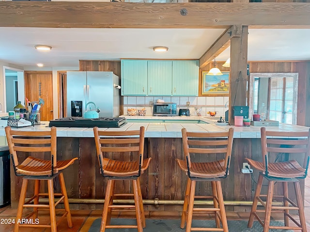 kitchen featuring appliances with stainless steel finishes, a breakfast bar area, kitchen peninsula, backsplash, and tile countertops