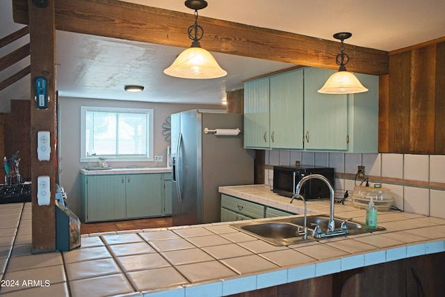 kitchen featuring tasteful backsplash, black microwave, tile countertops, stainless steel refrigerator with ice dispenser, and a sink