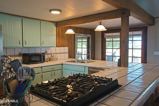 kitchen with green cabinetry, beam ceiling, a sink, black appliances, and tile counters