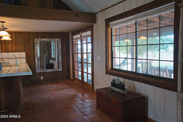 doorway to outside featuring beamed ceiling, wood walls, and a sink