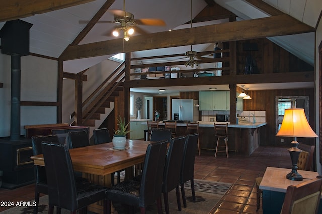 dining space featuring stairway, vaulted ceiling with beams, a wood stove, and a ceiling fan