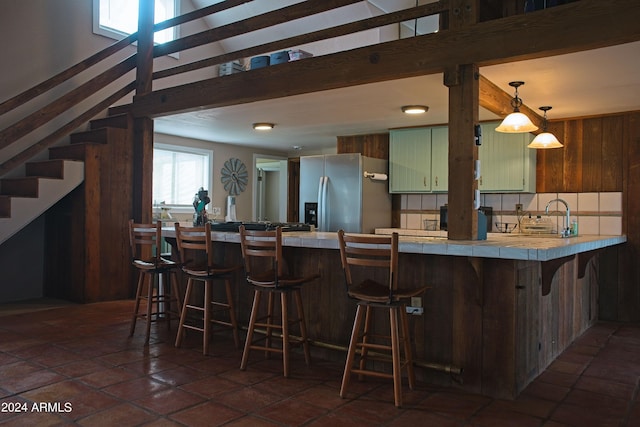 kitchen featuring beamed ceiling, a kitchen bar, stainless steel refrigerator with ice dispenser, tile countertops, and a peninsula