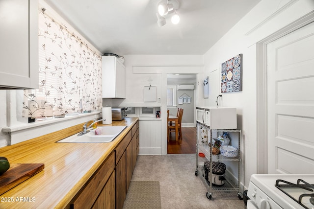kitchen featuring a wall mounted AC, white cabinetry, a sink, white appliances, and baseboards