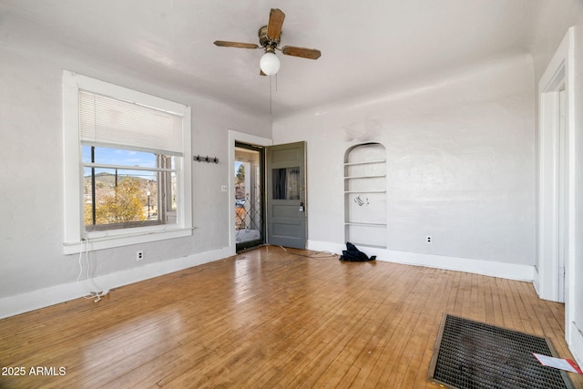 unfurnished living room with built in shelves, baseboards, ceiling fan, and hardwood / wood-style floors