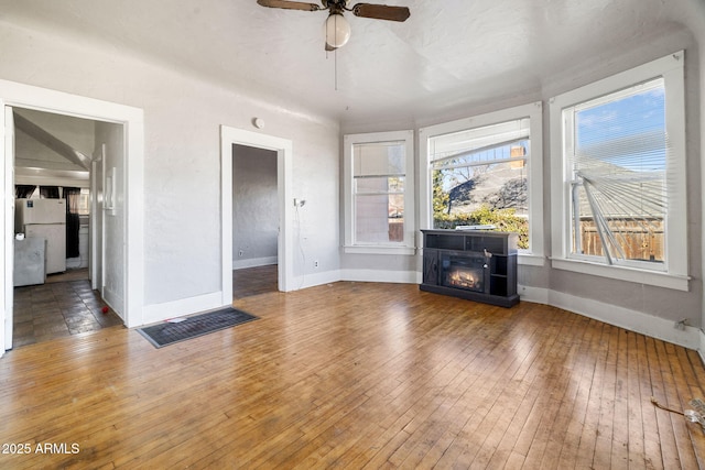 unfurnished living room with wood-type flooring, baseboards, a ceiling fan, and a glass covered fireplace