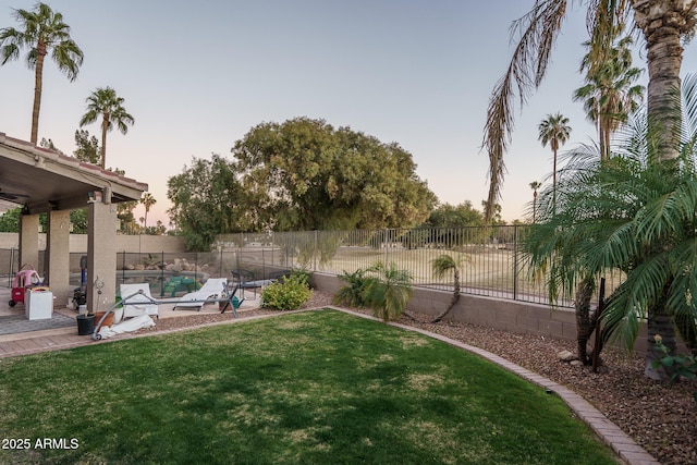 yard at dusk with a patio, a swimming pool, and a fenced backyard