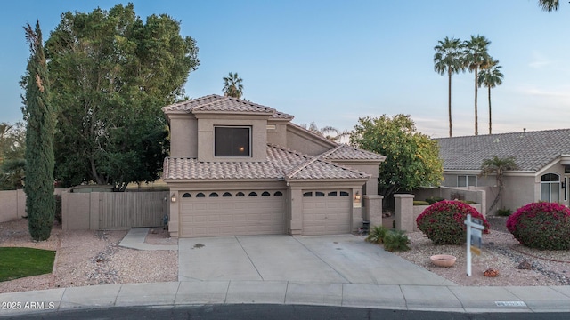 mediterranean / spanish-style home with a tile roof, fence, concrete driveway, and stucco siding