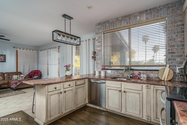 kitchen featuring cream cabinetry, appliances with stainless steel finishes, open floor plan, a sink, and a peninsula