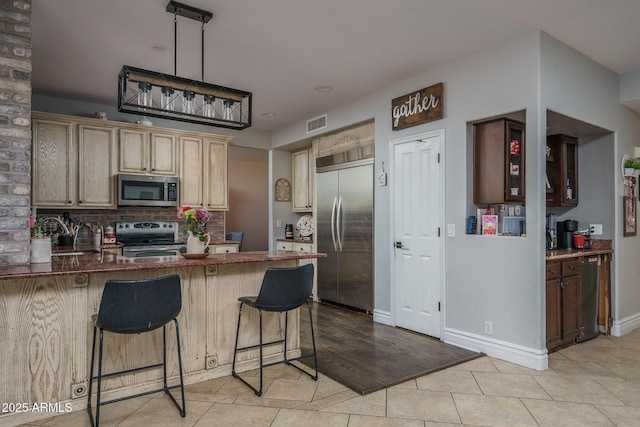 kitchen with visible vents, appliances with stainless steel finishes, a breakfast bar area, a peninsula, and light tile patterned flooring