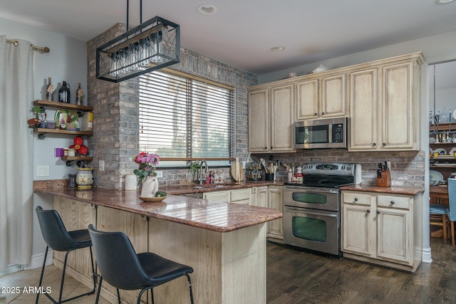 kitchen with dark wood finished floors, appliances with stainless steel finishes, backsplash, a peninsula, and a sink