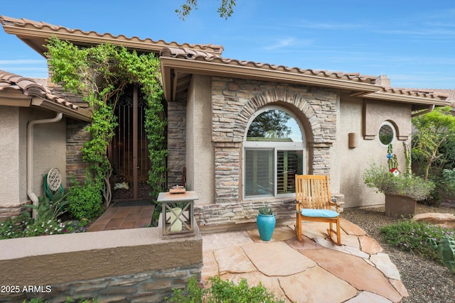 property entrance with a patio area, a tiled roof, stucco siding, and stone siding