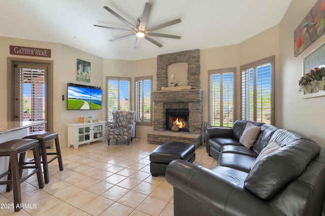 living room featuring a healthy amount of sunlight, light tile patterned floors, a ceiling fan, and a stone fireplace