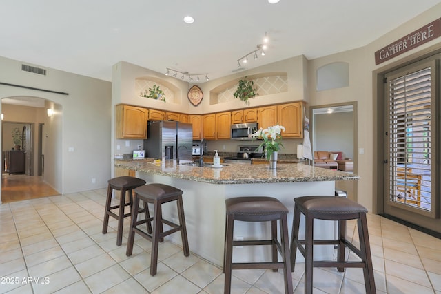 kitchen featuring light tile patterned floors, a kitchen breakfast bar, arched walkways, stone countertops, and stainless steel appliances