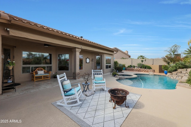 view of pool with a patio, a fire pit, a ceiling fan, a pool with connected hot tub, and fence