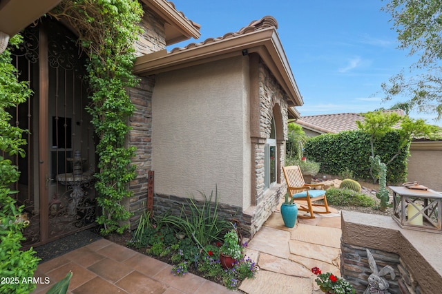view of side of property with a patio area, stucco siding, stone siding, and a tile roof