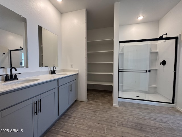 bathroom featuring a shower stall, double vanity, a sink, and wood tiled floor