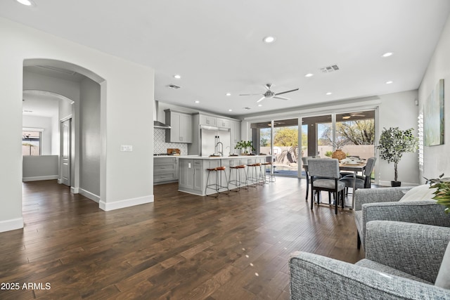 living area with arched walkways, dark wood-style flooring, plenty of natural light, and visible vents