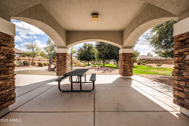 view of patio featuring playground community and fence