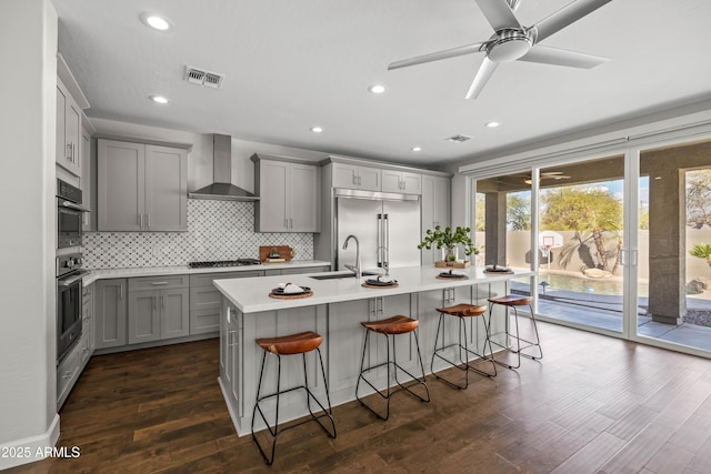 kitchen with stainless steel appliances, visible vents, gray cabinetry, a sink, and wall chimney exhaust hood