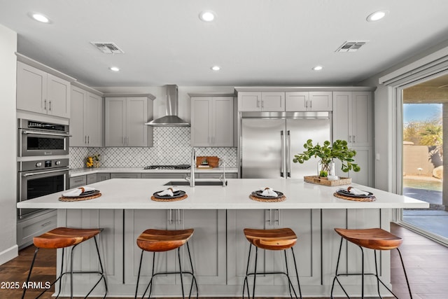 kitchen with stainless steel appliances, gray cabinets, and wall chimney exhaust hood