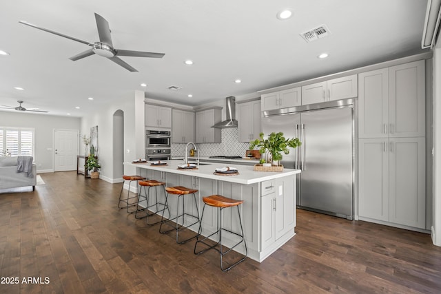 kitchen featuring arched walkways, gray cabinetry, visible vents, appliances with stainless steel finishes, and wall chimney exhaust hood