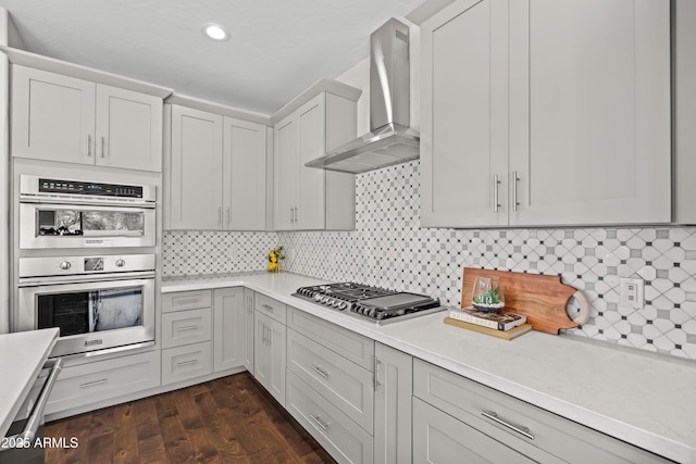 kitchen with appliances with stainless steel finishes, dark wood-style flooring, light countertops, and wall chimney exhaust hood