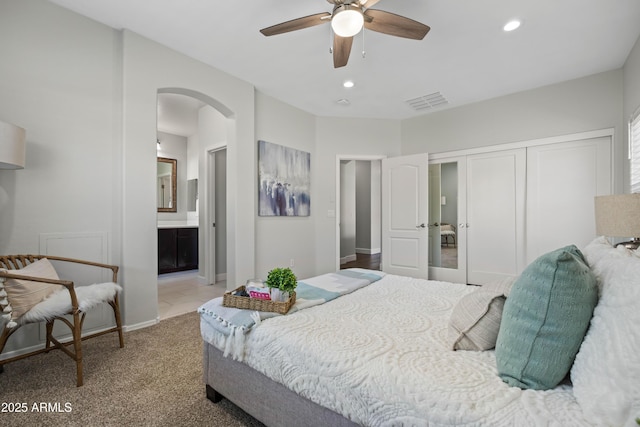 carpeted bedroom with arched walkways, recessed lighting, a closet, visible vents, and connected bathroom