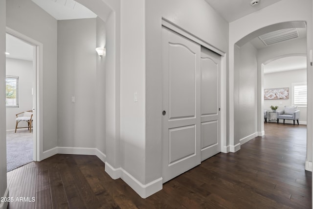 hallway with dark wood-style floors, baseboards, visible vents, and arched walkways