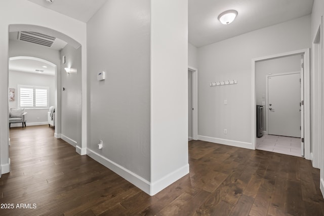 hall featuring hardwood / wood-style flooring, baseboards, visible vents, and arched walkways