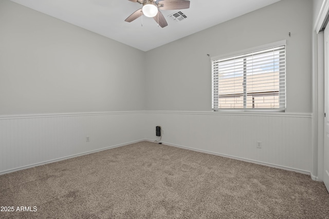 empty room with carpet floors, wainscoting, and visible vents