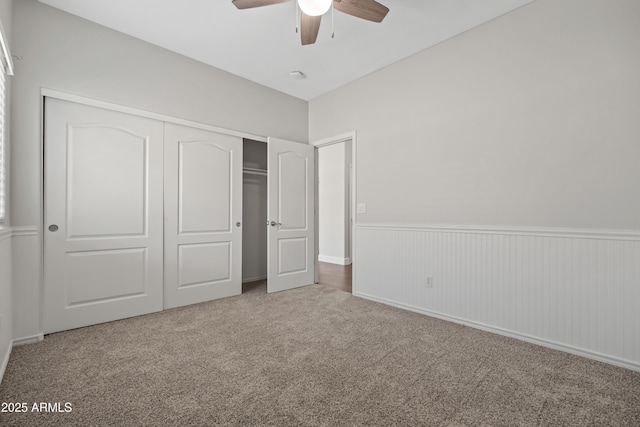 unfurnished bedroom with carpet, a closet, a wainscoted wall, and ceiling fan