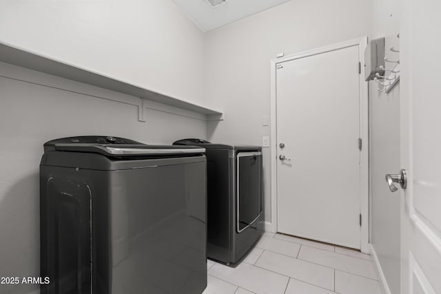 clothes washing area featuring washer and dryer, laundry area, light tile patterned flooring, and baseboards