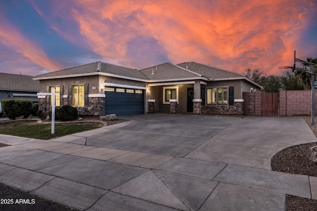 prairie-style house with stone siding, an attached garage, fence, and stucco siding