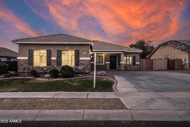 view of front of home with stone siding, fence, a tiled roof, and stucco siding