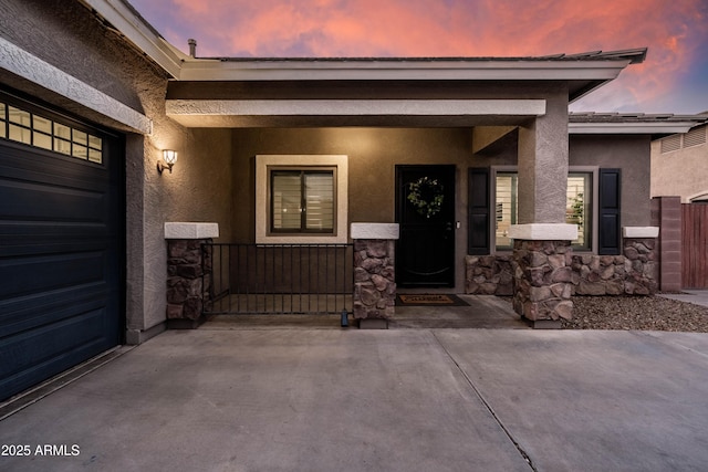 exterior entry at dusk with a porch, stone siding, and stucco siding