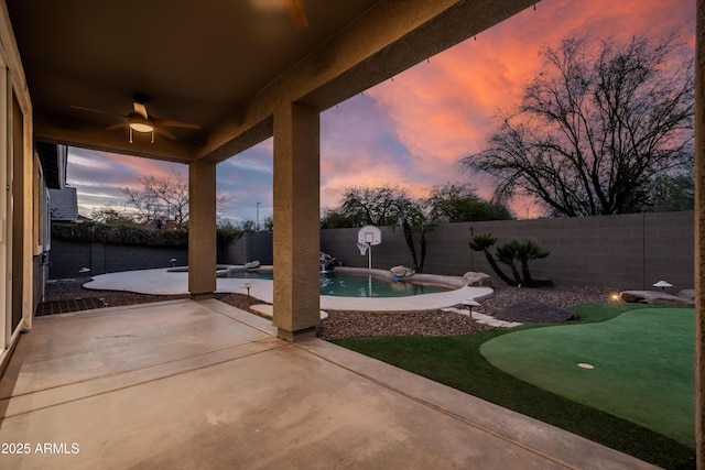 patio terrace at dusk with a fenced in pool, a fenced backyard, and ceiling fan