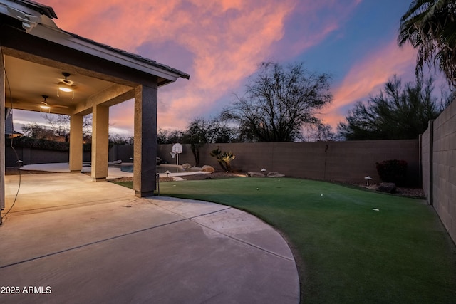 yard at dusk with a ceiling fan, a fenced backyard, and a patio