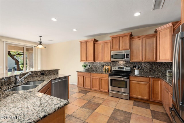 kitchen with stone counters, appliances with stainless steel finishes, decorative light fixtures, and sink