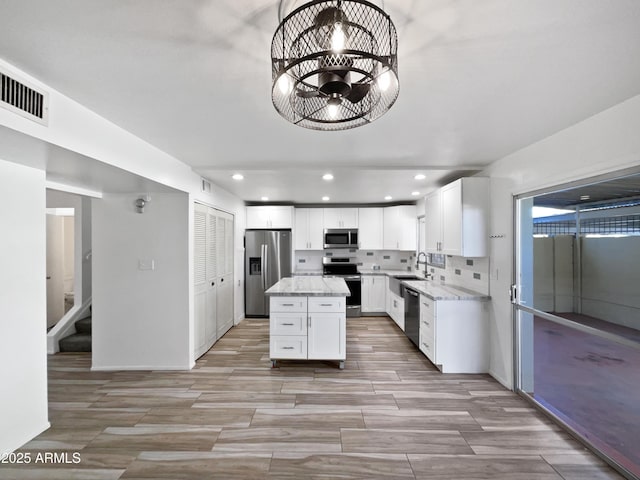 kitchen with light stone countertops, sink, a kitchen island, white cabinets, and appliances with stainless steel finishes