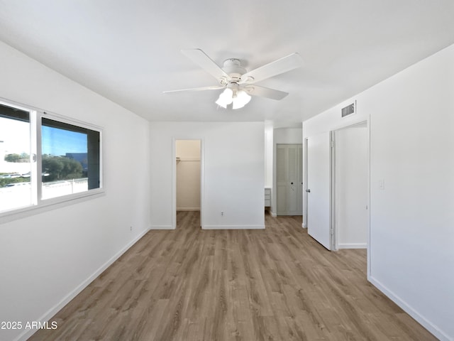 unfurnished bedroom featuring a walk in closet, light hardwood / wood-style flooring, and ceiling fan