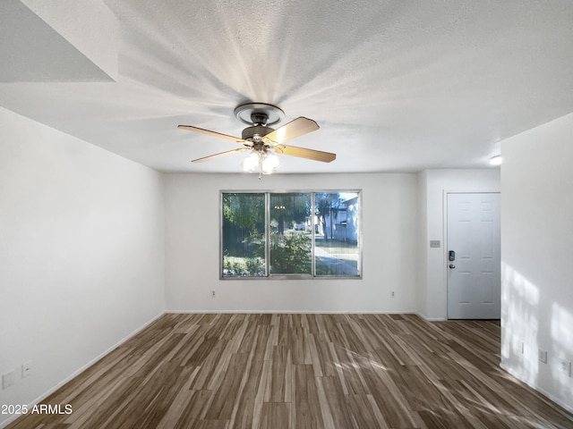 empty room with ceiling fan, dark wood-type flooring, and a textured ceiling